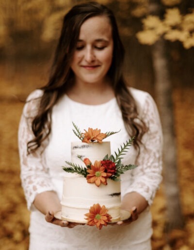 A bride holding her two-tiered chocolate wedding cake with white icing with orange flowers.